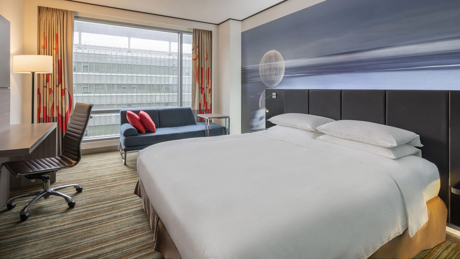 A king bed, blue sofa and desk by the window in a Deluxe Room