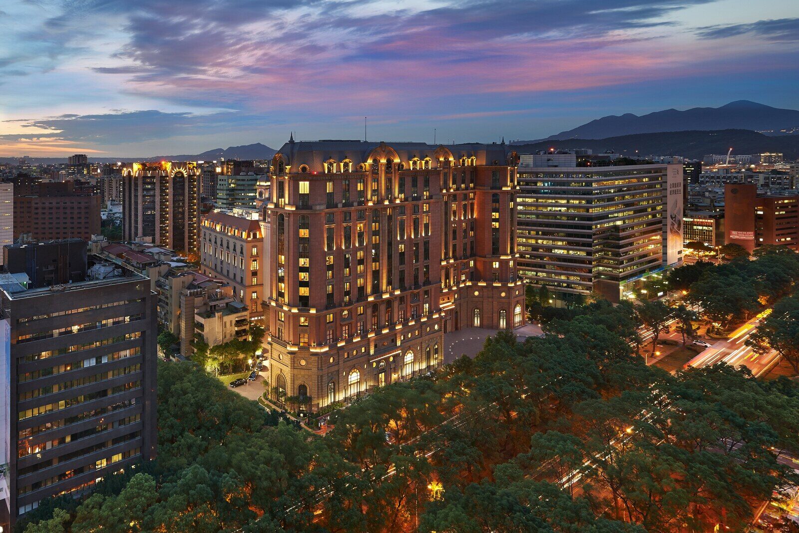The European-style exterior of Mandarin Oriental, Taipei at dusk, with street trees along Dunhua North Road