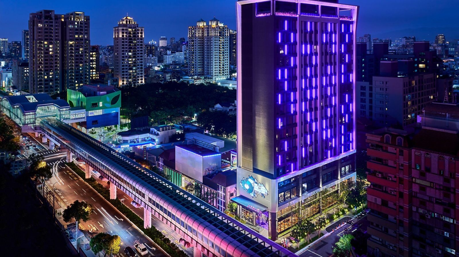 The hotel tower lit in purple at night, beside the elevated MRT line and downtown Taichung buildings