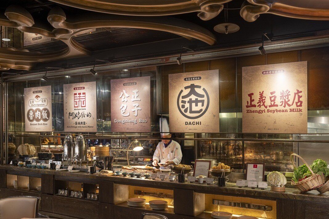 Shop-name signboards such as Zhengyi Soy Milk (正義豆漿) and Gongzheng Baozi (公正包子) hanging above the breakfast buffet