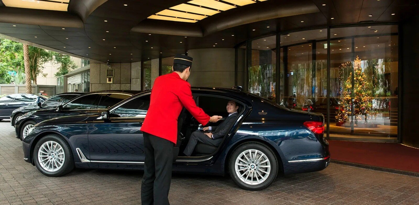 A black sedan under the hotel porte-cochère with a doorman in a red uniform