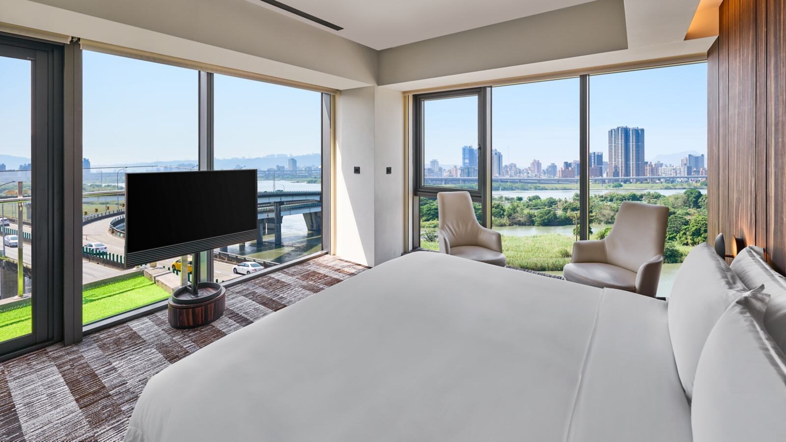 River Corner Suite 的大床、電視與兩側落地窗外的河岸景色