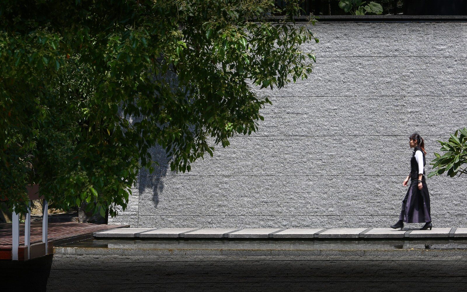 A path beside a grey stone wall in the shade of trees