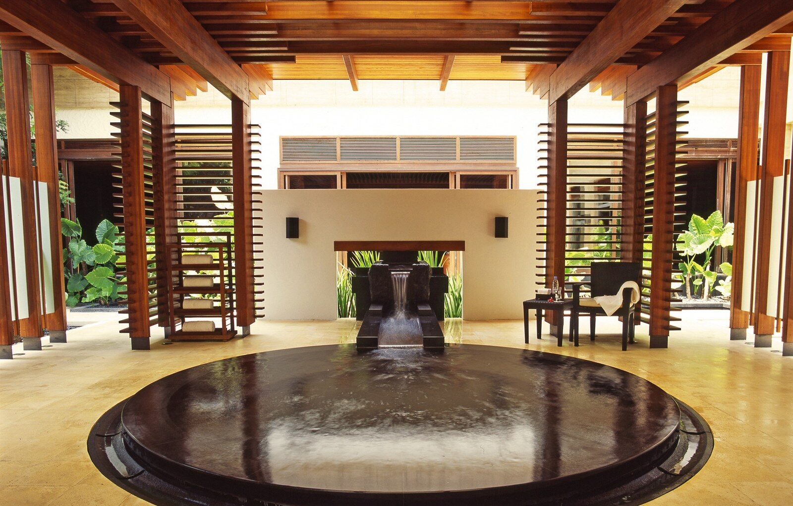 A round hot spring pool and stone water spout under a timber roof